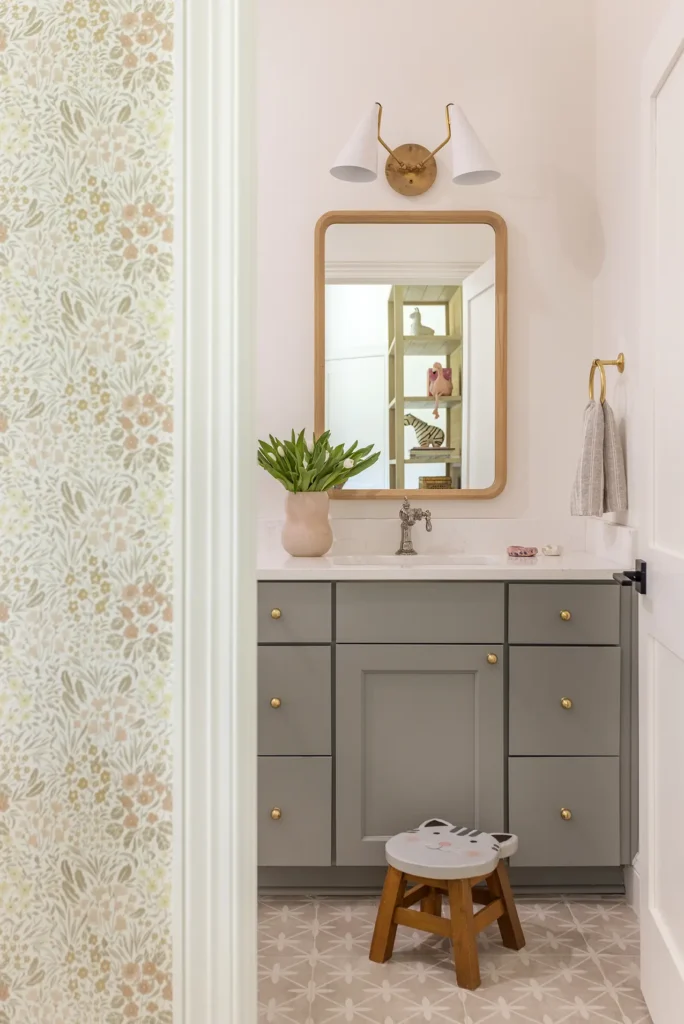 Charming kids’ bathroom renovation with sage green vanity, floral wallpaper, and gold accents in Ponte Vedra custom home by Alesch.
