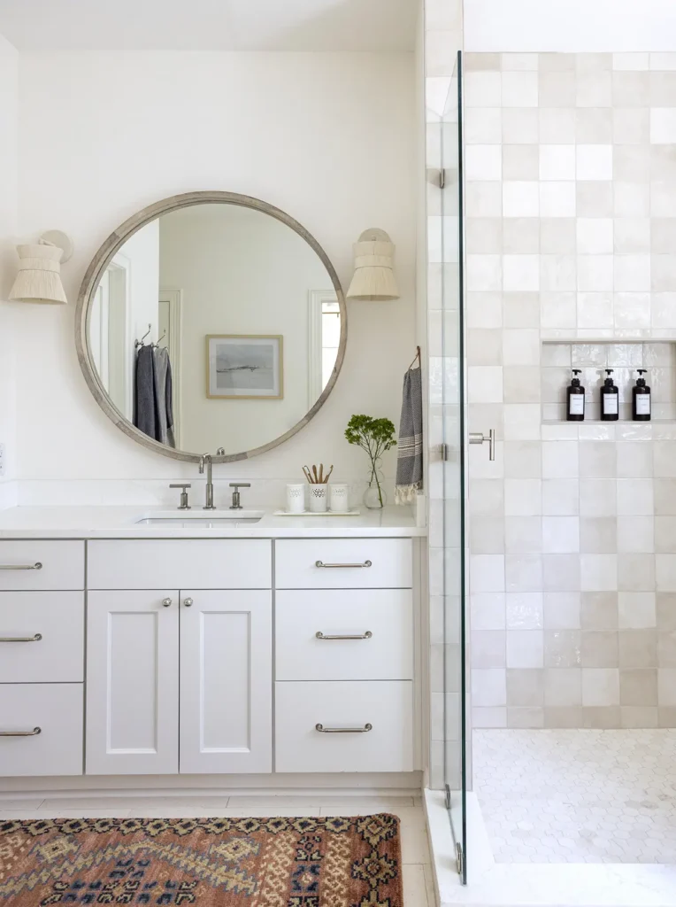 Serene master bathroom with round mirror, glass walk-in shower, and handmade tile in custom home design Ponte Vedra renovation by Alesch Luxury Custom Builders