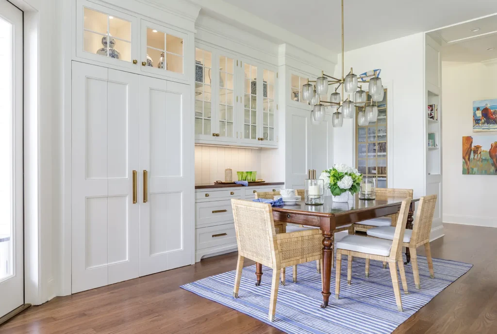 Refined dining room remodel featuring glass cabinetry, cane chairs, and statement lighting in Ponte Vedra Beach. Dining room and kitchen renovation by Alesch Luxury Custom Builders.