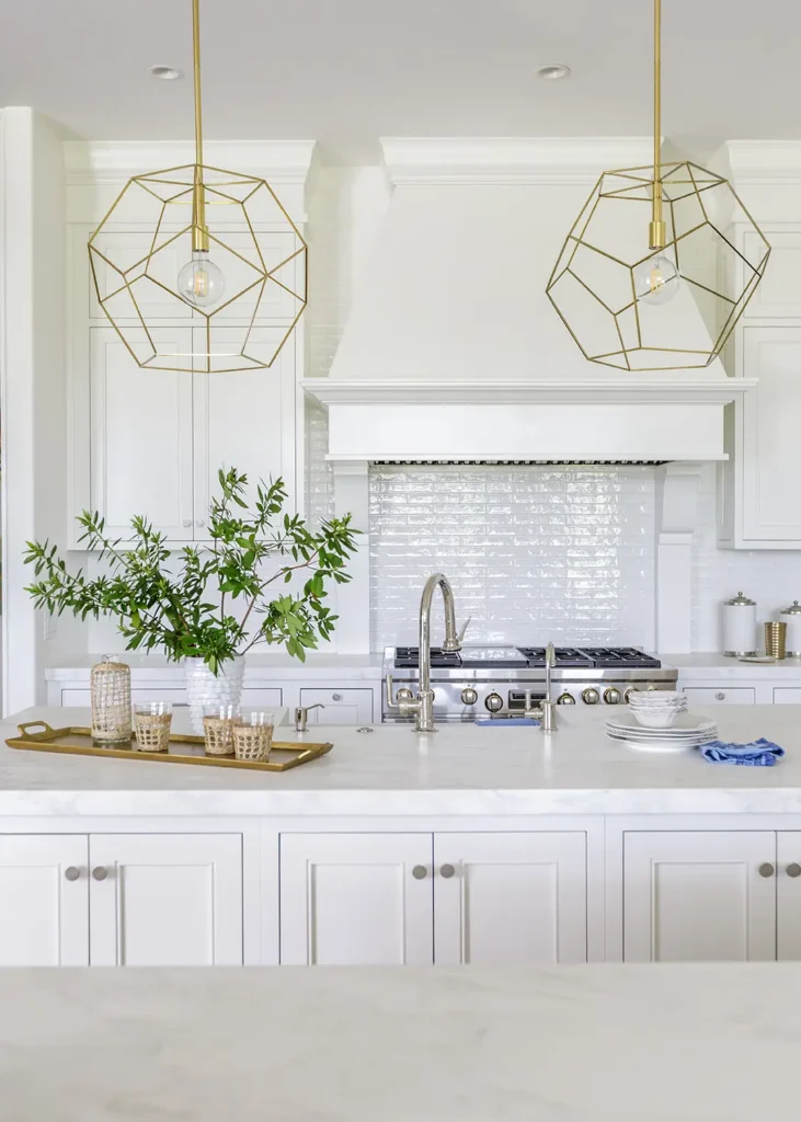 Bright white kitchen renovation in Ponte Vedra with geometric gold pendant lights, modern white cabinetry, and large center island with polished nickel fixtures.