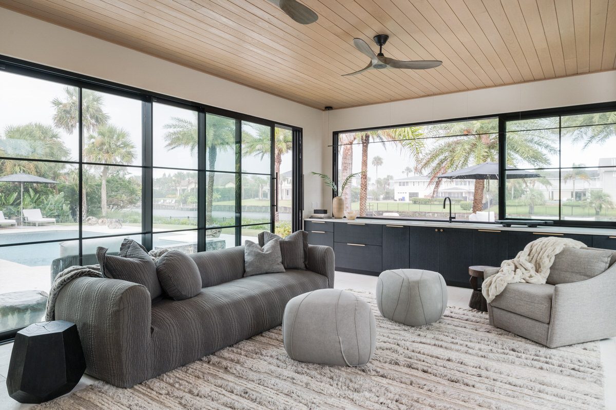 design build living room pool view jacksonville alesch Living room with wood plank ceiling and black steel windows opening to a pool, by Alesch design build firm in the Jacksonville area