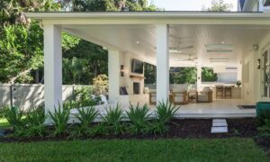 Covered outdoor living room addition with white columns, fireplace, and lush landscaping by Alesch, home addition builder in Jacksonville Beach