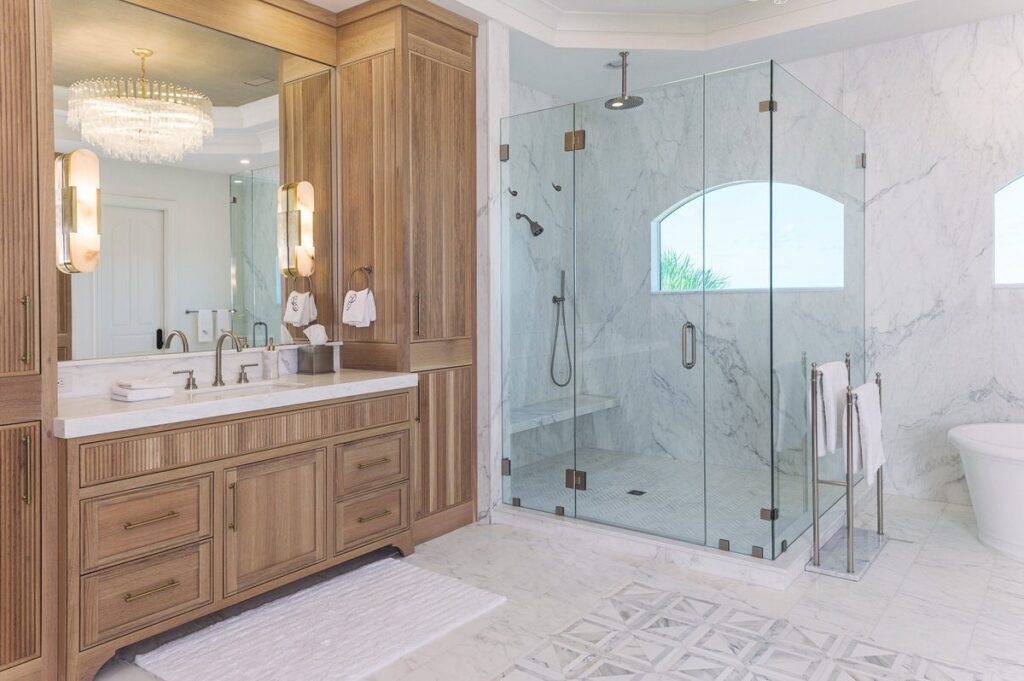 Renovated primary bathroom with white oak vanity, marble walk-in shower, and crystal chandelier from a luxury home renovation by Alesch, serving Ponte Vedra Beach